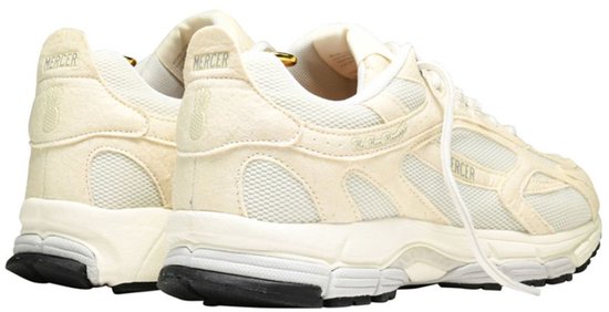 Crème Mercer sneakers, achterzijde. "MERCER" logo en ananas-detail op de hakken. Zwarte zolen met verfspatten.