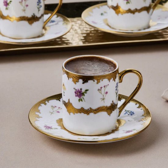 Porseleinen Turkse koffiekopje met schotel, wit met kleurrijke bloemen en gouden details, gevuld met koffie.