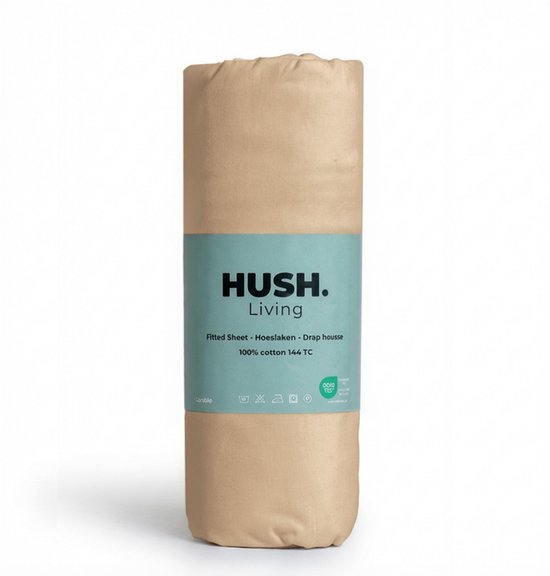 Zandkleurig hoeslaken opgerold met een groen label waarop 'HUSH. Living', 'Fitted Sheet - Hoeslaken - Drap housse', '100% cotton 144 TC'.