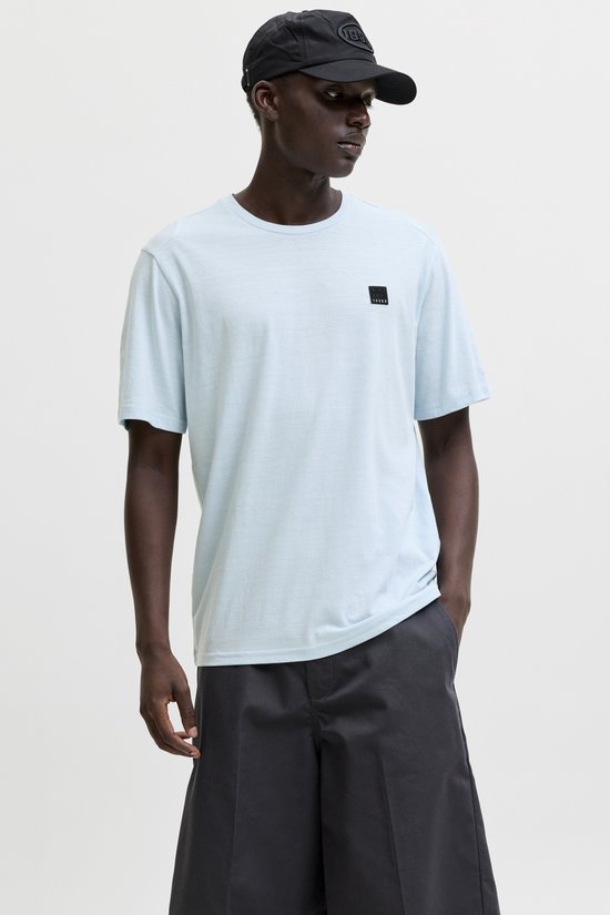 Man met donkere huid draagt lichtblauwe t-shirt en grijze shorts, met zwarte pet.