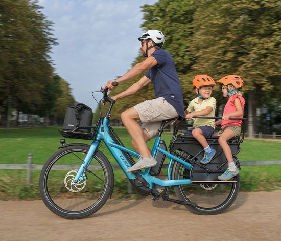 Man met twee kinderen op een lichtblauwe Cube e-bike met kinderzitjes en een tas op de bagagedrager.