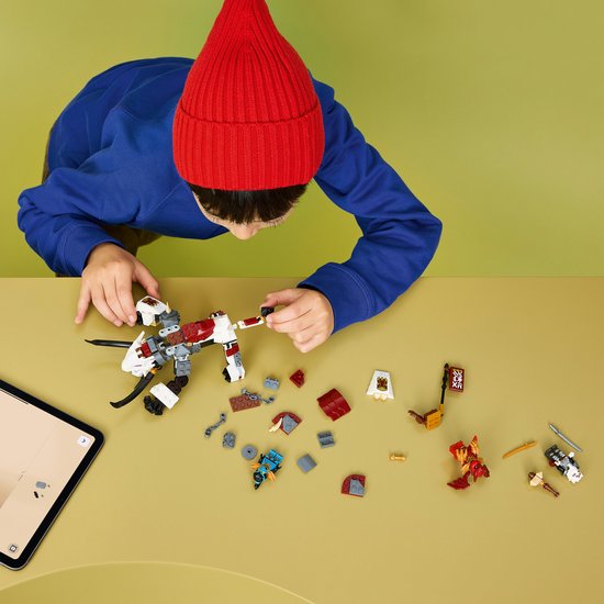 Jongen met rode muts bouwt LEGO NINJAGO speelgoed op een tafel, met een draak, rode draak en losse onderdelen.