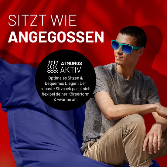 Een man met een t-shirt en zonnebril zit op een grote, donkerblauwe zitzak. Hij kijkt naar de zijkant.