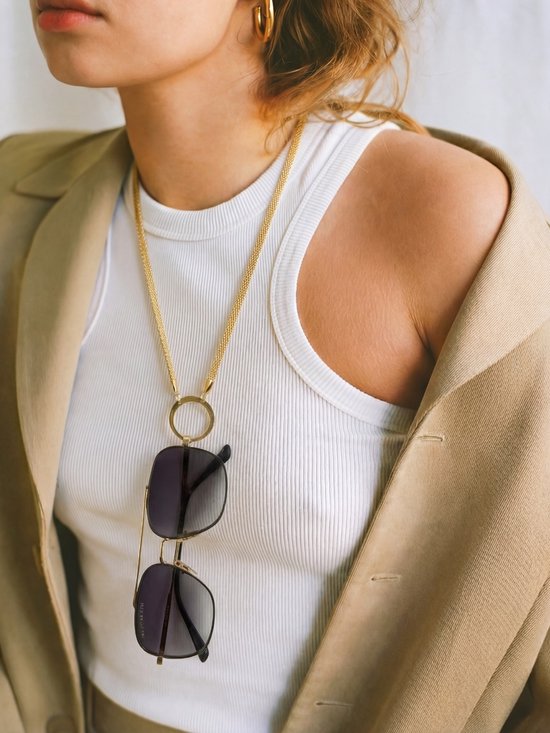 Gouden ketting met zonnebril, gedragen door model met beige blazer en witte tanktop.