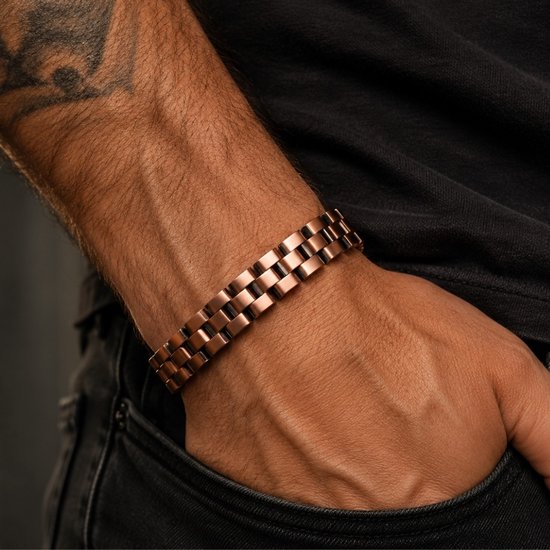 Man met tatoeage draagt een koperkleurige armband met schakels om de pols.