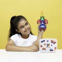 Meisje met een raket gemaakt van Connetix magnetische tegels in regenboogkleuren, naast een witte koffer met stickers.