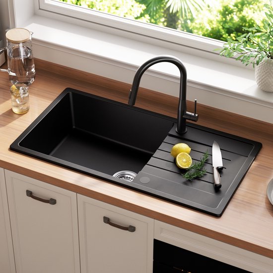 Évier noir avec robinet, une planche à découper avec des citrons et du romarin, et une carafe d'eau.