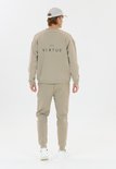 Man in beige trainingsbroek en sweater, rugzijde, met logo op de sweater.