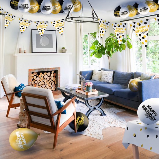 Feestelijke woonkamer met slingers, ballonnen en een gedekte tafel in zwart, wit en goud thema.