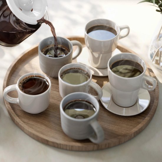 Une verseuse en verre verse du café chaud dans cinq tasses blanches et grises sur un plateau en bois.