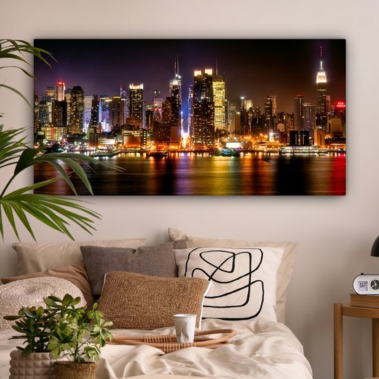 Une chambre avec un lit double et une toile panoramique de la skyline de New York la nuit comme décoration murale.