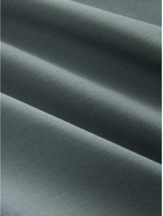 Detail van de stof van een donkergroen poloshirt, met zichtbare textuur en plooien.