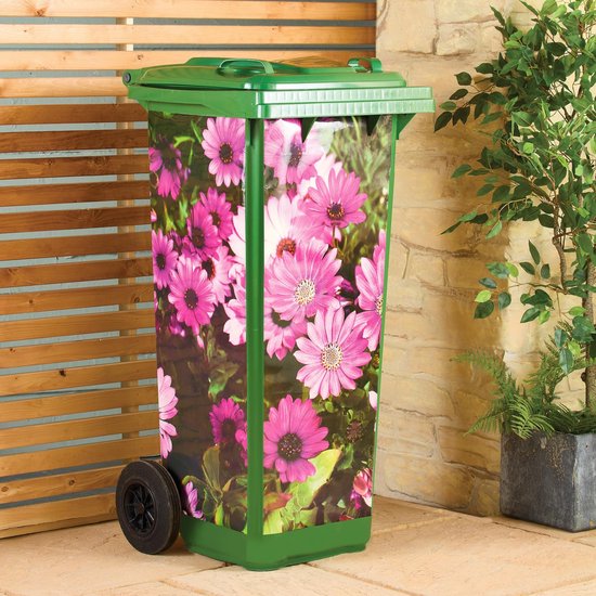 Groene afvalbak met roze bloemenprint, in een tuin met houten schutting en planten.