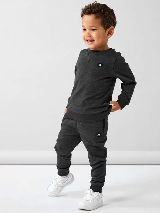Jongetje in donkergrijs joggingpak met witte logo's op sweater en broek.