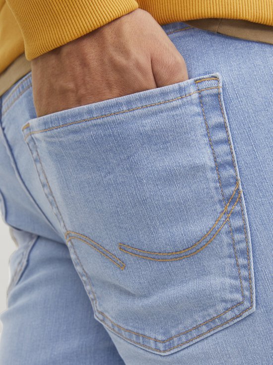 Detailopname van een achterzak van een lichtblauwe jeans met opvallende bruine stiksels.
