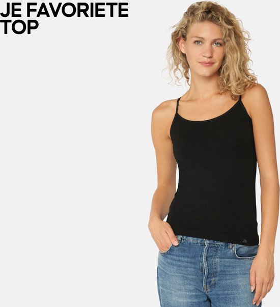 Vrouw met krullend blond haar draagt een zwart hemdje met spaghettibandjes en een spijkerbroek.