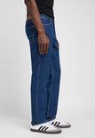 Man met donkerblauwe jeans, zichtbaar vanaf de zijkant. Lee-logo op de tailleband.