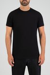 Man met baard draagt een zwart T-shirt met ronde hals en donkere jeans.