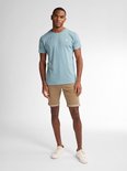 Man met bruine slim fit shorts en een lichtblauw T-shirt met subtiele textuur.