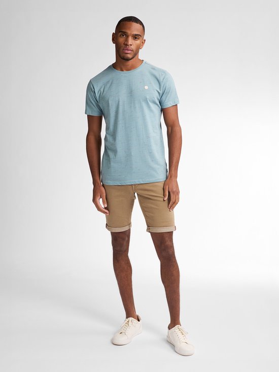 Man met bruine slim fit shorts en een lichtblauw T-shirt met subtiele textuur.