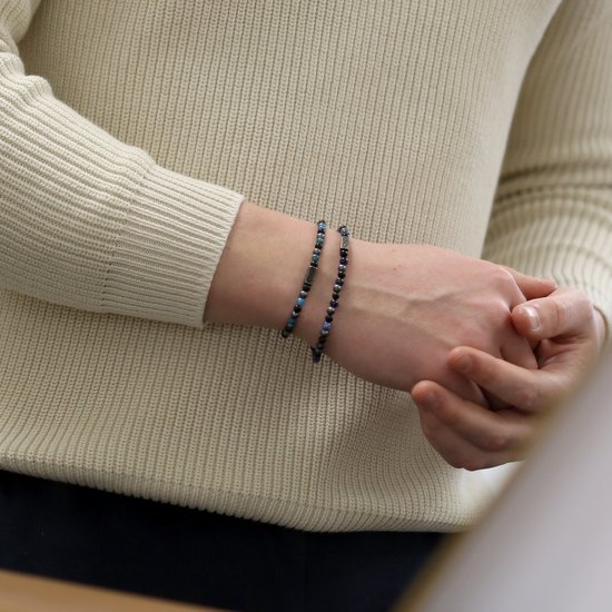 Een man draagt twee blauw-grijze kralenarmbanden met een infinity symbool.