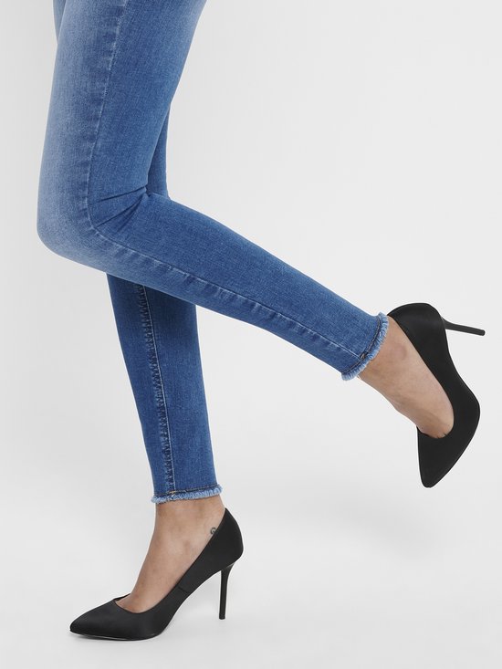Close-up van een model die een skinny jeans draagt met rafelige zoom en zwarte pumps.