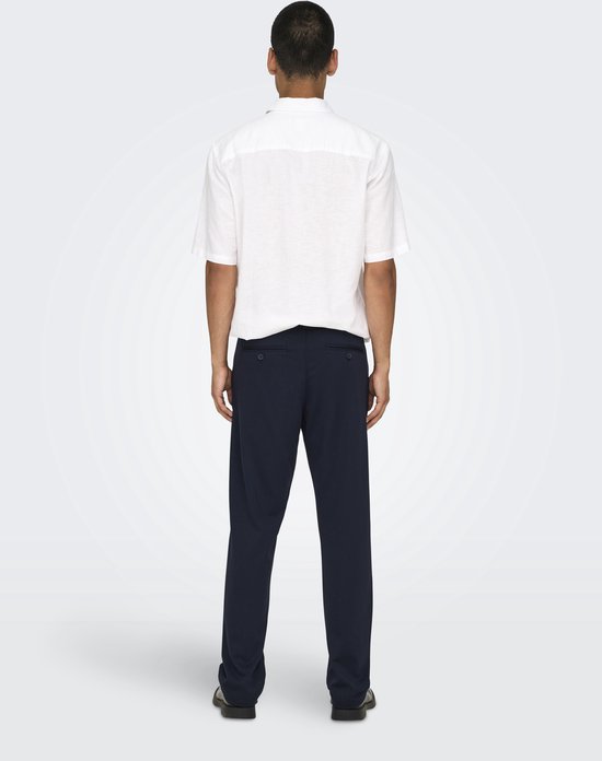 Man draagt donkere broek en wit hemd, achterkant.