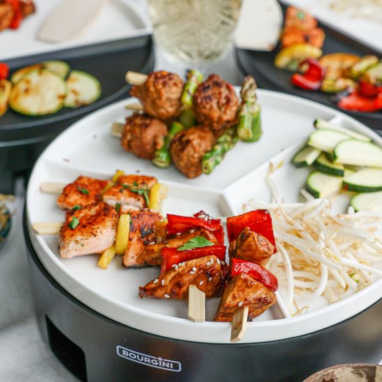 Gourmetstel met diverse spiesjes, vlees, vis en groenten op een gedeeld bord.