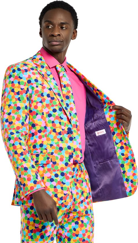 Man in een veelkleurig pak met confettiprint, roze shirt en paarse voering.