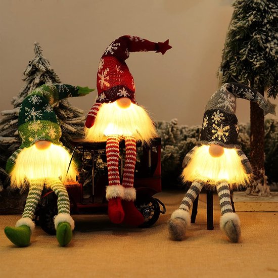 Trois gnomes de Noël éclairés. À gauche un vert, au milieu un rouge et à droite un gris, assis devant des sapins de Noël.