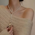 Crèmekleurige parelketting met een gouden bloemvormige hanger met zirkoon en parelmoer, gedragen door een vrouw met een beige trui.