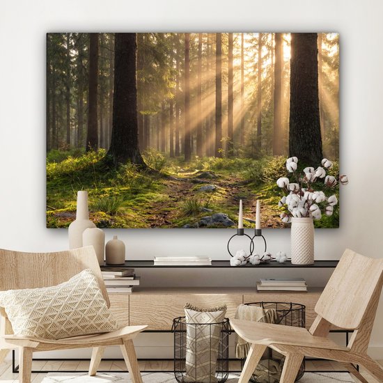 Een woonkamer met een canvas schilderij van een bos met zonlicht. Voor de bank staan stoelen en een kastje met decoraties.