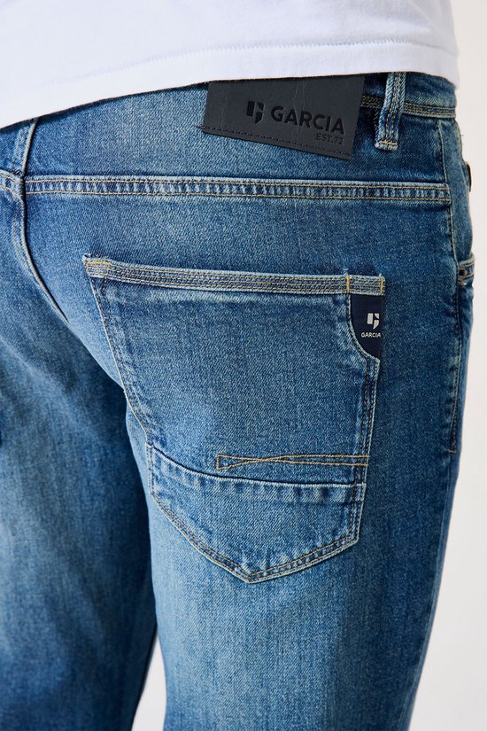 Detail van de achterkant van een blauwe jeans met een zwart label van Garcia 'EST. 72'.