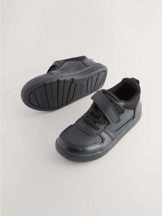 Een paar zwarte, leren sneakers met klittenbandsluiting, wit gestikt, op een witte achtergrond.