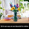 Een boeket van Lego-bloemen in een glazen vaas op een houten tafel, met een tekst die suggereert dat het een decorstuk is.