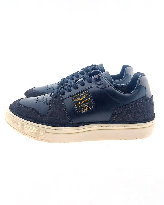 Baskets en cuir noir avec empiècements en daim, semelles blanches et badge jaune sur le côté.