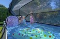 Vrouw met baby en kind in rechthoekig zwembad met afdak, met speelgoed in het water.