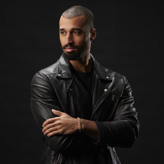 Man met baard, zwarte leren jas, draagt een gouden schakelarmband.