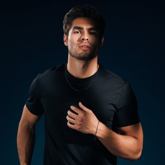 Man met zwart T-shirt draagt een dunne zwarte ketting en een zwarte armband met bedeltje.