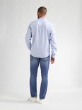 De achterkant van een man in een lichtblauwe spijkerbroek en witte sneakers. Het model draagt een lichtblauwe blouse.