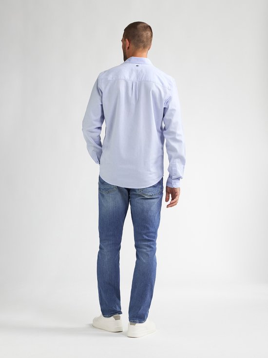 De achterkant van een man in een lichtblauwe spijkerbroek en witte sneakers. Het model draagt een lichtblauwe blouse.