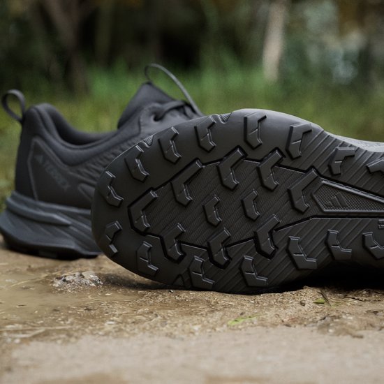 Zwarte Adidas Terrex trailrunningschoen met profielzool, op een ondergrond van zand en gras.