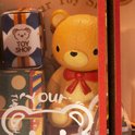 Gedetailleerde close-up van een teddybeer met rode strik in een miniatuur speelgoedwinkel.