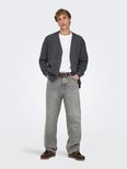 Een man draagt een grijze jeans met rechte pijpen, een wit shirt, een grijze vest en bruine instappers.