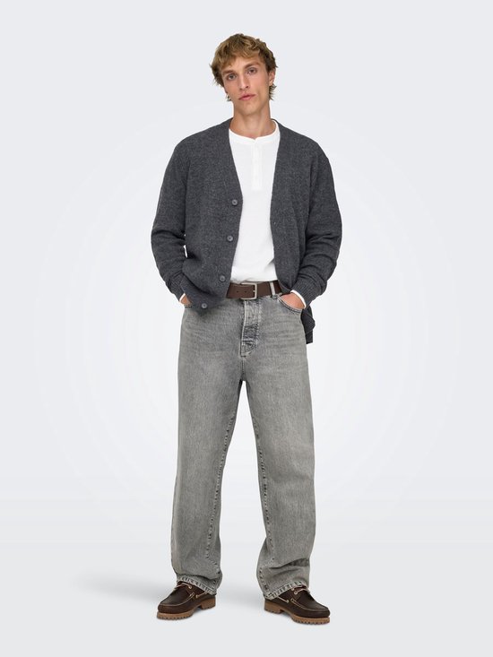 Een man draagt een grijze jeans met rechte pijpen, een wit shirt, een grijze vest en bruine instappers.