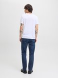 Jonge man met tatoeages, staand met de rug naar de camera in een witte T-shirt en donkere jeans.
