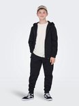 Jongen in crème T-shirt, zwarte joggingbroek en zwart vest met capuchon.