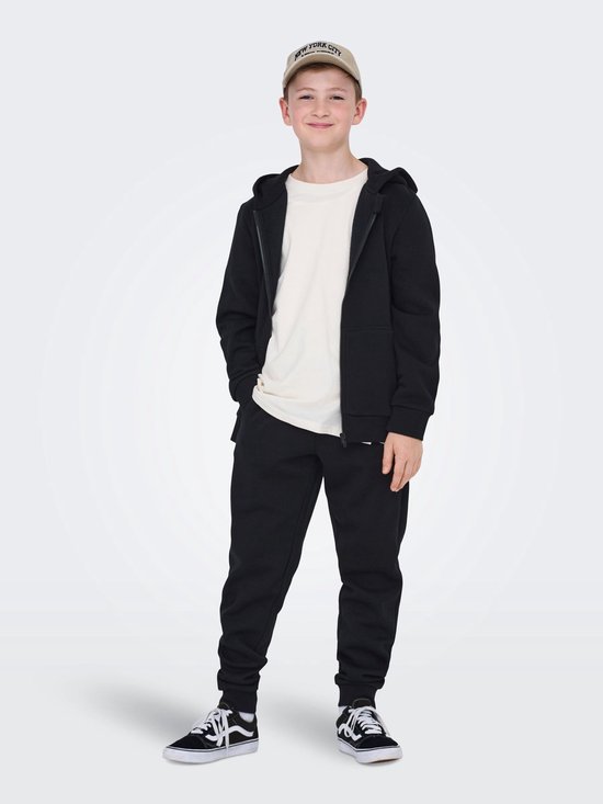 Jongen in crème T-shirt, zwarte joggingbroek en zwart vest met capuchon.