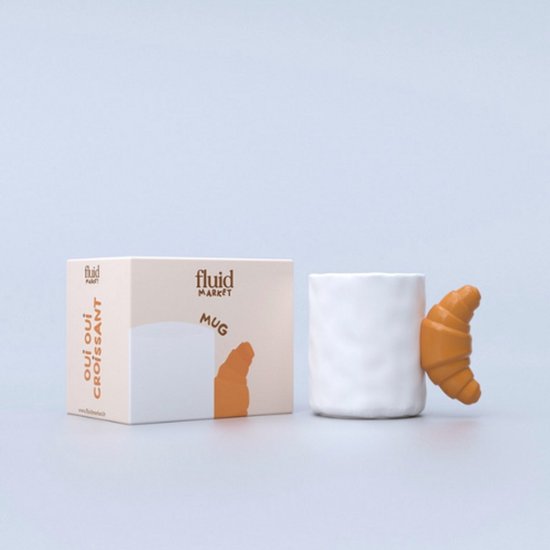 Witte mok met een bruin-oranje croissant als oor, naast de verpakking met 'Oui oui Croissant' tekst.