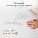 Une femme s'étire sur un lit avec un surmatelas à imprimé bambou et le logo OEKO-TEX.